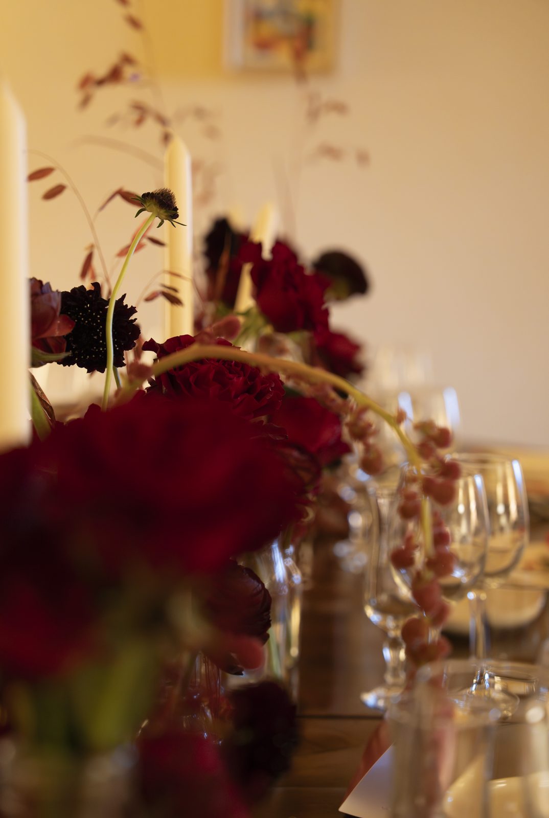 Composizione floreale bordeaux con candele e calici di cristallo